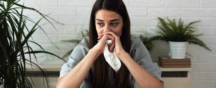 Young brunette woman sitting at table crying with tissues